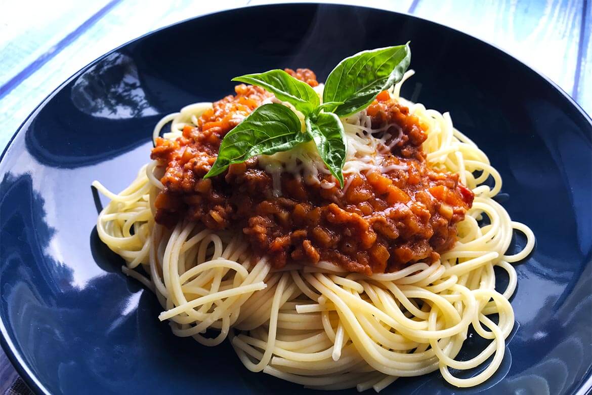 bolonské špagety s lístkami bazalky na tmavomodrom tanieri