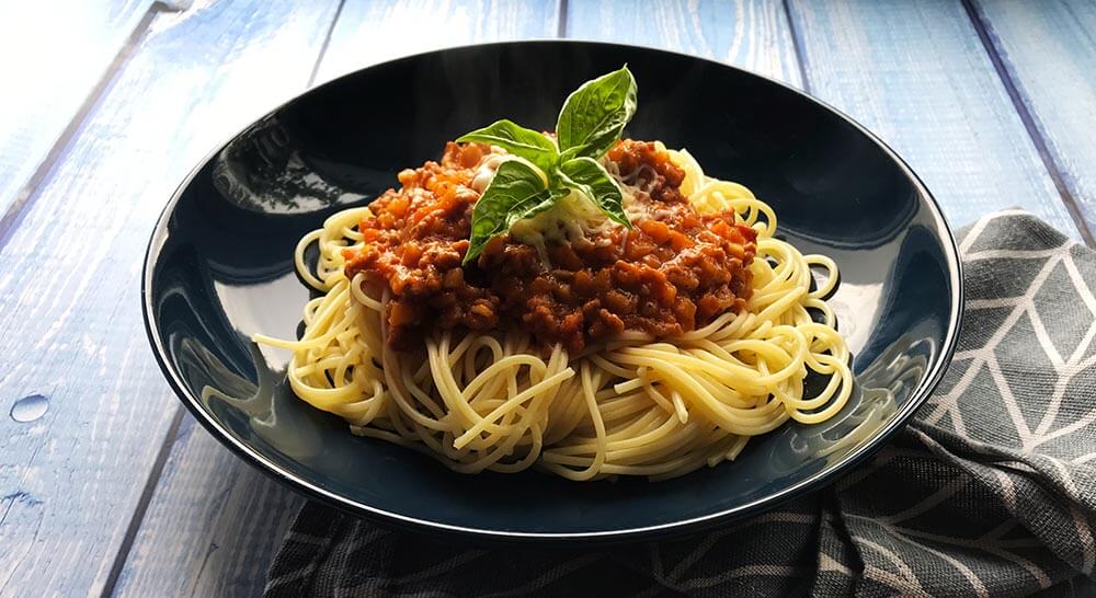 bolonské špagety s lístkami bazalky servírované v tmavomodrom tanieri