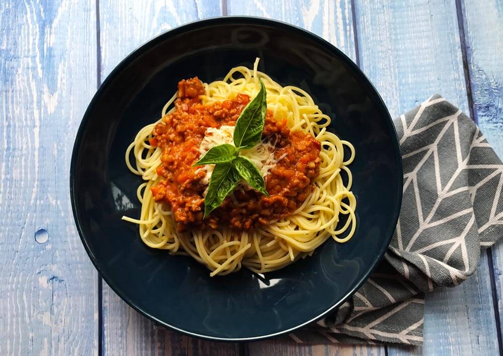 špagety s bolonským ragú a lístkami bazalky servírované v tmavomodrom tanieri